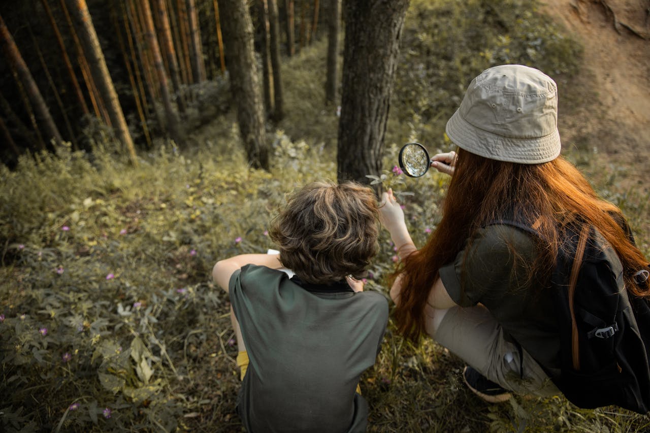 Two teenagers exploring the forest with a magnifying glass, enjoying outdoor adventure.