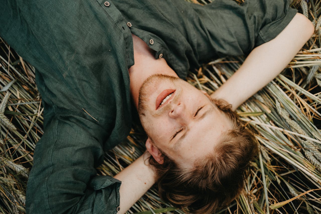 A man enjoying tranquility with closed eyes, lying on grassy terrain, capturing a serene moment.
